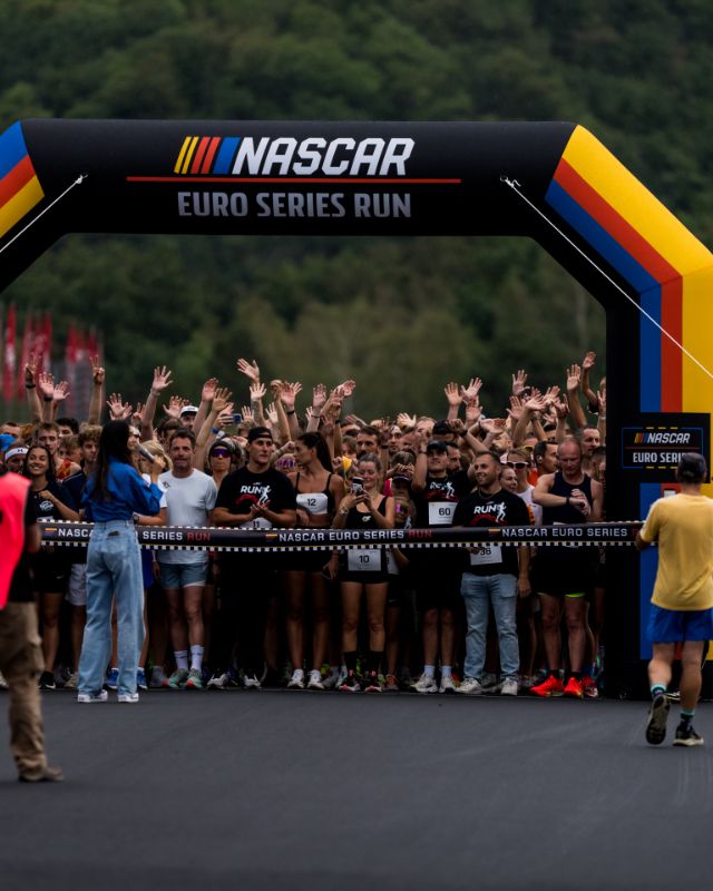 Runners raise hands behind tape under NASCAR start arch