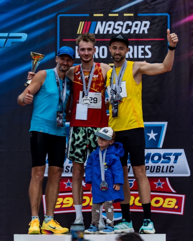 Three podium finishers and a child, trophy raised
