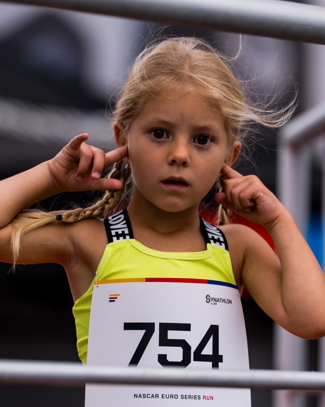 Young girl wearing bib 754 behind metal railing